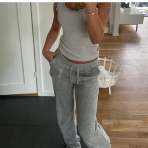 Grå mjukisbyxor Juicy Couture - Supermysiga grå mjukisbyxor från Juicy Couture med broderad logga på benet och bred resår i midjan. Byxorna har snörning och är tillverkade i mjuk bomullsblandning. Perfekta för chill dagar eller när du vill vara extra bekväm.