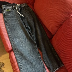 Svarta baggy fit jeans med snörning - Säljer ett par svarta jeans med extra baggy fit och hög midja. Jeansen har en cool snörning i midjan istället för vanlig knapp och dragkedja. Klassisk femficksmodell och raka ben. Perfekta för en avslappnad streetstil.