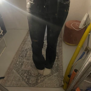 Svarta jeans med slitningar och glitter - Snygga svarta jeans med diskreta slitningar på låret och coola nitar vid fickorna. Jeansen har en bootcut passform och klassisk femficksdesign. Materialet är stretchigt jeans och färgen är tvättad svart med lite gråton. 