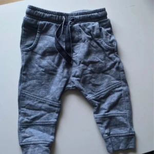 Blå mjukisbyxor från Newbie, stl 68 barn - Mysiga blå mjukisbyxor från Newbie i storlek 68. Byxorna har resår i midjan med snörning, två fickor fram och en bakficka. Tillverkade i mjukt bomullstyg, perfekta för chill dagar. Snygga sömdetaljer på benen.