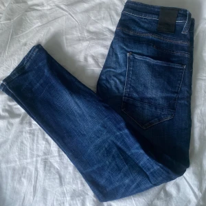 Jack & Jones Mörkblå  jeans - Snygga mörkblå jeans med passform och klassiska fem fickor. Jeansen har en lätt tvättad look och kontrastsömmar. Perfekta till sneakers eller boots och funkar året runt.