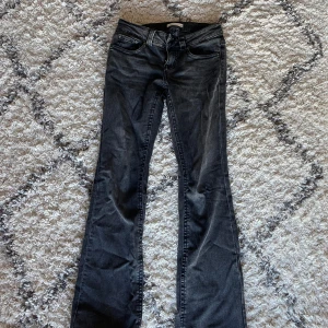 Svarta bootcut jeans från Gina Tricot - Snygga svarta bootcut jeans från Gina Tricot med lätt tvättad look. Modellen har låg midja, klassiska fem fickor och silverfärgade knappar. Jeansen är i stretchigt denim och har en figurnära passform upptill som går ut i bootcut nedtill.