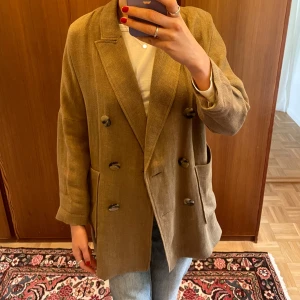 Beige kavaj från Zara Woman, stl S - Snygg beige kavaj från Zara Woman i storlek S. Dubbelknäppt modell med stora knappar och två rejäla fickor framtill. Kavajen har en rak, lite loose passform och är tillverkad i ett strukturerat tyg som ger en cool och avslappnad look.