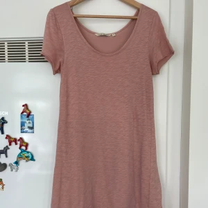 Rosa kortklänning från House of Lola - Superfin och jätteskön  rosa klänning  från House of Lola med rund halsringning och korta ärmar. Klänningen har en snygg slits bak och en liten metallbricka med logga vid fållen. Perfekt för dig som gillar enkel och skön klänning i mjukt tyg. 