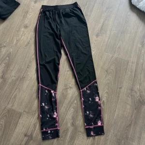 Svarta underställsbyxor  med rosa mönster. - Snygga svarta underställsbyxor med rosa sömmar och blommigt mönster på nedre delen av benen. Stretchigt material som sitter tight och är perfekt för träning eller chill. Midjan är elastisk för extra komfort.