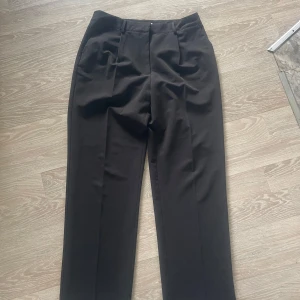 Svarta kostymbyxor med pressveck - Snygga svarta kostymbyxor med klassiska pressveck och rak passform. Byxorna har hällor för bälte och diskreta fickor bak. Har andvänts fåtal gånger och är i mycket bra skick 
