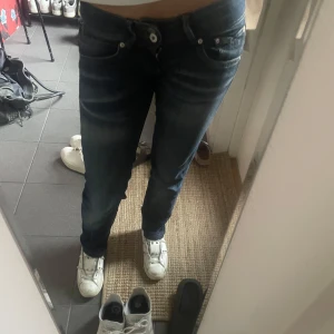 Mörkblå lågmidjade jeans  - Säljer ett par mörkblå jeansbyxor med klassisk femficksdesign. Byxorna har låg midja och raka ben, med snygga slitningar och kontrastsömmar.