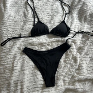 Svart bikini från H&M - Säljer en klassisk svart bikini från H&M. Överdelen är trekantsmodell med knyt i rygg och nacke, och underdelen har en hög midja. Tillverkad i stretchigt material som består av polyamid och elastan. Överdelen är i storlek 38 och underdelen är i storlek 34 