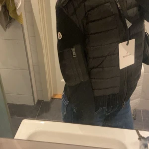 Svart pufferjacka från Moncler - Säljer en svart pufferjacka från Moncler med dragkedja framtill och ribbade muddar. Jackan har lång ärm, quiltade partier och Moncler-logga på ärmen. Perfekt för kyligare dagar och snygg till jeans. Storlek M , men passar som S