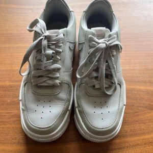 Nike Air Force 1 Pixel vita sneakers - Säljer ett par vita Nike Air Force 1 sneakers med klassisk design och dubbla detaljer. Skorna har snörning, rund tå och är tillverkade i skinn med vit sula. Perfekta för dig som gillar stilrena och tidlösa sneakers.