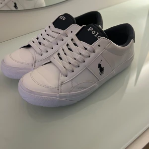 Vita sneakers från Polo Ralph Lauren - Säljer ett par fräscha vita sneakers från Polo Ralph Lauren med svart detalj vid hälen och klassisk logga på sidan. De är endast använda två gånger då dom tyvärr är för små för mig så säljer jag dom, så väldigt bra skick!
