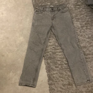 Grå jeansbyxor från Grunt köpt för 800kr - Säljer ett par grå jeansbyxor från Grunt med klassisk femficksdesign och raka ben. Byxorna har normal passform och stängs med knapp och dragkedja. Perfekta till en avslappnad stil.