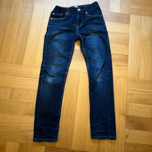 Levi's 512 Slim Taper jeans - Mörkblå Levi's 512 jeans med slim taper passform. Klassisk femficksdesign, synliga nitar och kontrastsömmar. Ikonisk läderpatch bak i midjan och Levis-röd etikett på bakfickan. Perfekta för en stilren och modern look.