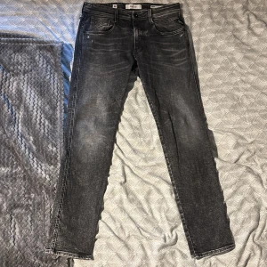  Replay anbass jeans - Säljer ett par svarta Replay jeans med slitna detaljer och klassisk femficksdesign. perfekt för dig som gillar en stilren look. Snygga kontrastsömmar och knappgylf. Dem är köpta för 1899kr och är i mycket bra skick. Skriv vid frågor eller vid diskution om pris!