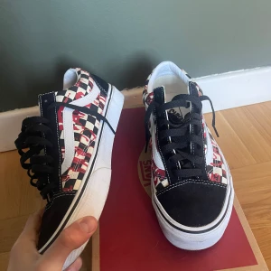 Vans Old Skool graffity  - Säljer ett par Vans Old Skool med svart mocka, vit sula och klassisk vit sidosnöre. Skorna har ett schackrutigt mönster i svart och beige med röd graffiti färg. Svarta skosnören och vit kant runt sulan. Använd endast 1 gång, (skick 9/10)