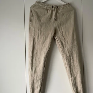 Beiga mjukisbyxor från CJP Leisurewear - Säljer ett par beiga mjukisbyxor från CJP Leisurewear i storlek XS. Byxorna har resår och snörning i midjan samt raka ben. Perfekta för en avslappnad stil och tillverkade i mjukt material.