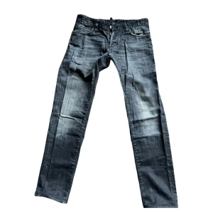 Svarta jeansbyxor från Dsquared2 - Säljer ett par svarta jeansbyxor från Dsquared2 med snyggt slitna detaljer och klassisk femficksdesign. Byxorna har raka ben och normal passform, perfekt för dig som gillar en stilren look med lite edge.