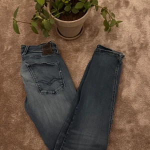 Blå Replay Anbass jeans - Säljer ett par blå Replay Anbass jeans i storlek 32. med snygga slitningar och Replay logga på bakfickan. Perfekta jeans för dig som gillar en modern och stilren look.