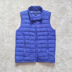 Blå Ralph Lauren väst - Stl L 14-16 - Hej säljer en snygg Ralph Lauren väst i färgen blå. Fint skick, förutom att mitten dragkedjan inte fungerar. Går säkert att lösa hos en skräddare.😊 Storleken är L 14-16 och passar XS/S. Västen är endå snygg och man kan ha den hängandes utan att den är ihop. Passar dig bäst mellan 155-168cm. Han på bilden är 170cm och är lite för liten fast det inte syns så bra i bilden. 🤗 Hör av dig om du har några frågor. 
