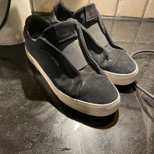 Svarta sneakers från Axel Arigato - Stilrena svarta sneakers från Axel Arigato med vit platt sula och elastisk panel över vristen. Skorna har en minimalistisk design utan snörning och är tillverkade i mocka. Perfekta för dig som gillar enkel och clean stil. Dock är skon rätt sliten eftersom att den är använd ett tag men ett nypris med 2650kr kan du knappast slå mitt pris med 350kr med box och påse🔥🤯