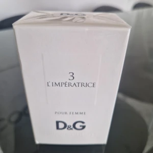 D&G 3 L'Impératrice Pour Femme Eau de Toilette - D&G 3 L'Impératrice Pour Femme är en elegant parfym i en vit kartongförpackning. Flaskan innehåller 50 ml eau de toilette och har en fräsch, feminin doft. Förpackningen är stilren med svart text och klassisk D&G-logga.