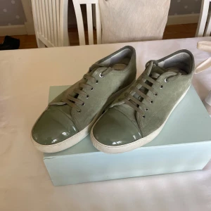 Olivgröna sneakers från Lanvin - Säljer ett par olivgröna sneakers från Lanvin med snygg snörning och rund tå. Skorna har en unik glansig tådel i samma färg och en vit platt sula. Perfekta för dig som vill ha något stilrent men ändå sticker ut. Box ingår