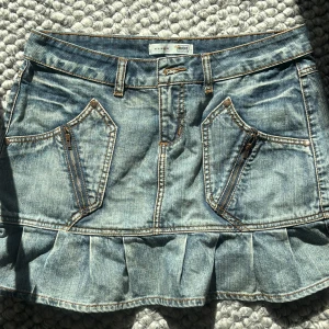 Jeanskjol med volang från True Object - Säljer en ljusblå jeanskjol från True Object med volang nertill och snygga dragkedjedetaljer på fickorna framtill. Kjolen har femficksdesign och sömmar på bakfickorna. Perfekt inför sommaren. Midjemått 41 cm