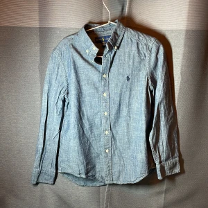 Blå skjorta från Polo Ralph Lauren - Klassisk blå skjorta från Polo Ralph Lauren. Skick 7,5/10. Storlek 10-12 år passar från 140 till 150 cm. Vi stryker den innan vi fraktar.