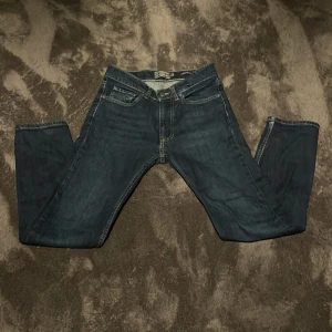 Mörkblå jeansbyxor från Dressmann - Säljer ett par klassiska mörkblå jeans från Dressmann i modellen regular fit. Byxorna har fyra fickor, gylf med dragkedja och knapp samt kontrastsömmar. Perfekta för en stilren och enkel look. Storlek 29/30.