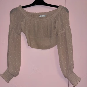 Rosa kort blus från NA-KD - Säljer en rosa blus från NA-KD med prickigt mönster. Blusen har långa ärmar med resår vid ärmslut och axelbandslös offshoulder-modell. Perfekt för vår och sommar! Syns dåligt på bilden men den är rosa använd få tal gånger🫶🏼
