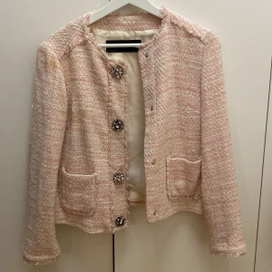 Ljusrosa tweedjacka från Zara Basic - Säljer en ljusrosa tweedjacka från Zara Basic med dekorativa stora knappar och två fickor framtill. Jackan har lång ärm och är fodrad, perfekt för en chic look. Klassisk rak modell med fina detaljer. Smutsig och behöver en tvätt.