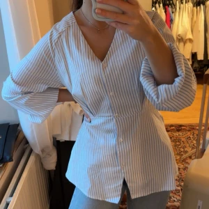 Blåvit randig blus med v-ringning - Säljer en blåvit randig blus med v-ringning och långa ärmar. Blusen har knappar framtill och en markerad midja som ger en snygg siluett. Perfekt till jeans för en fräsch look. Storlek 34 men passar mig som bär S och M 🌸🌸