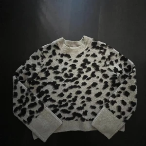 stickad leopardmönstrad tröja - Säljer en stickad tröja med svart leopardmönster. Tröjan har rund halsringning och långa ärmar med breda ribbade muddar. Perfekt för dig som vill sticka ut lite extra i vardagen.