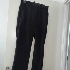 Svarta kostymbyxor - Snygga svarta kostymbyxor med lite vida ben och klassisk passform. Byxorna har hällor för bälte, diskreta fickor och stängs med dragkedja och hyska.