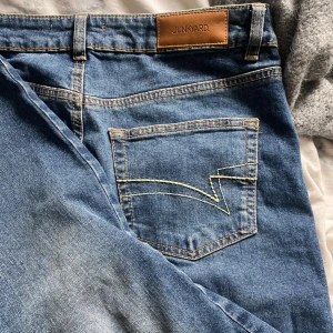 Blå jeans från Junkyard - Säljer ett par klassiska blå jeans från Junkyard med snygga kontrastsömmar och bakficka med unik sömdesign. Jeansen har normal passform och är perfekta till vardagslooken. Har bara provat så dom är andvänat 1 gång 