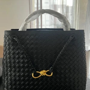 Svart handväska - Säljer en svart läder handväska i flätat skinn med guldfärgad metall-detalj framtill. Väskan har två handtag och en klassisk, elegant design som passar till många tillfällen. Alla logor är på rätt platser. Den är 32cm bred och 25cm hög så får plats med en laptop i och är användbar rymlig vardagsväska. Ej använd. Pris kan justeras vid snabb affär 🌸