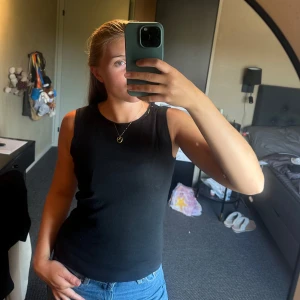 Svart ärmlös topp med paljettdetalj - Snygg svart ärmlös topp med rund halsringning och diskreta svarta paljetter längs kragen. Enkel och stilren modell som passar perfekt till jeans eller kjol. Mjuk och stretchig känsla.