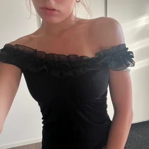 Svart volangtop från H&M - Supersöt svart topp från H&M med volangdetaljer i mesh längs urringningen. Toppen är ärmlös och kan bäras offshoulder för en extra snygg look. Tight passform som framhäver figuren och passar perfekt till jeans eller kjol💕thrifted i Polen 