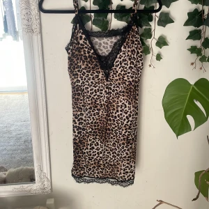 Leopardmönstrad kort slipklänning - Snygg kort slipklänning med leopardmönster och tunna axelband. Klänningen har v-ringning och svarta spetsdetaljer vid halsringning och nederkant. Perfekt för dig som vill sticka ut med en djurisk look.