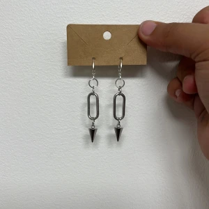 Silvriga örhängen med kedja och kon - Snygga silvriga örhängen med en avlång kedjelänk och en cool konformad detalj längst ner. Ger en edgy vibe och passar perfekt om du gillar statement-accessoarer. Metallisk finish och minimalistisk design.