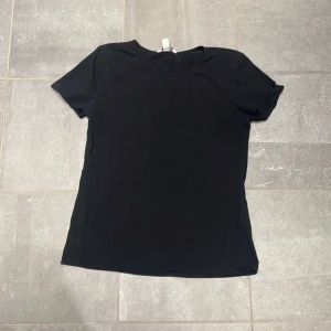 Svart basic t-shirt från H&M - En klassisk svart t-shirt från H&M med rund halsringning och korta ärmar. Modellen är enkel och passar perfekt till jeans eller shorts. Tillverkad i mjuk bomull för en skön känsla hela dagen. Går att diskutera pris.
