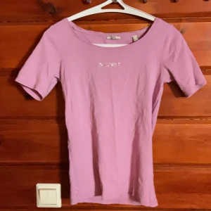 Ljusrosa topp från Esprit med strass - Supersöt ljusrosa topp från Esprit med korta ärmar och rund halsringning. Framtill står Esprit i glittriga strasstenar som ger en extra touch. Mjuk och skön bomullskvalitet, perfekt till jeans eller kjol.