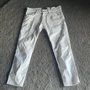 Vita jeansbyxor från Replay Anbass - Säljer ett par fräscha vita jeansbyxor från Replay, modell Anbass. Byxorna har klassisk femficksdesign, raka ben och normal passform. Perfekta för dig som vill ha en stilren och clean look. Märkesdetaljer på insidan och bak.