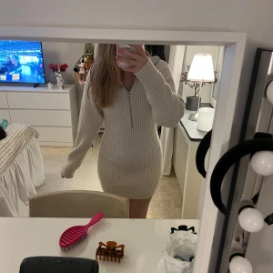 Beige ribbad stickad klänning H&M - Supermysig beige stickad klänning från H&M med ribbad struktur och lång ärm. Modellen är kort och har en snygg half zip-dragkedja framtill. Perfekt för lager på lager och chill dagar. Sitter tajt men ändå bekvämt.