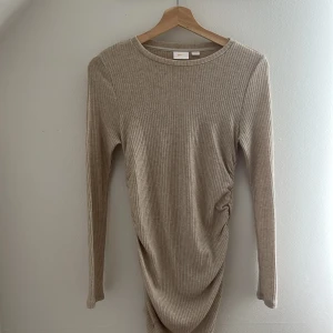 Beige ribbad klänning Gina Tricot - Superfin beige ribbad klänning från Gina Tricot med lång ärm och rund hals. Klänningen har en tight passform och snygg rynkdetalj på sidan som ger en cool look. Perfekt för dig som gillar stilrena och bekväma outfits.
