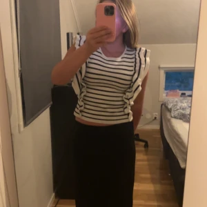 Randig blus med volang - Säljer en vit och svart randig blus med breda volangdetaljer längs axlarna. Toppen är ärmlös och har en rund halsringning. 