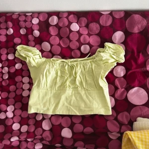 Limegrön croppad blus med puffärmar - Supersöt lime grön croppad blus med puffiga korta ärmar och smockad rygg. Toppen har en söt volangkant vid axlarna och en luftig, somrig känsla. Perfekt för dig som gillar romantisk och trendig stil.