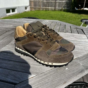 Valentino Rockrunner sneakers camouflage - Snygga Valentino Rockrunner sneakers med camouflage-mönster i grönt och brunt. Skorna har detaljer i mocka och skinn, samt coola nitar runt hälen. Grov sula och klassisk snörning. Perfekta för dig som vill sticka ut med exklusiva sneakers. Skick7/10