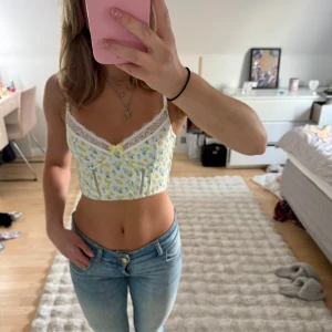 Blommig korsett med spets och rosett - Original pris 525 kr ! Supersöt korsett-topp i storlek 65C i vitt med små blå och gula blommor, spetskant upptill och en liten gul rosett i mitten🩷 Toppen är croppad och har justerbara axelband✨ Denna säljs då den är lite för liten på mig och har ändats används vid provning då varan kom till mig och för att ta bilderna som finns här på den 🩷