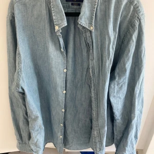 Ljusblå jeansskjorta Ralph Lauren XL - Snygg ljusblå jeansskjorta från Ralph Lauren i slim fit-modell. Skjortan har klassisk krage, knäppning framtill och broderad logga på bröstet. Tillverkad i mjukt bomullstyg och passar perfekt till jeans eller chinos.